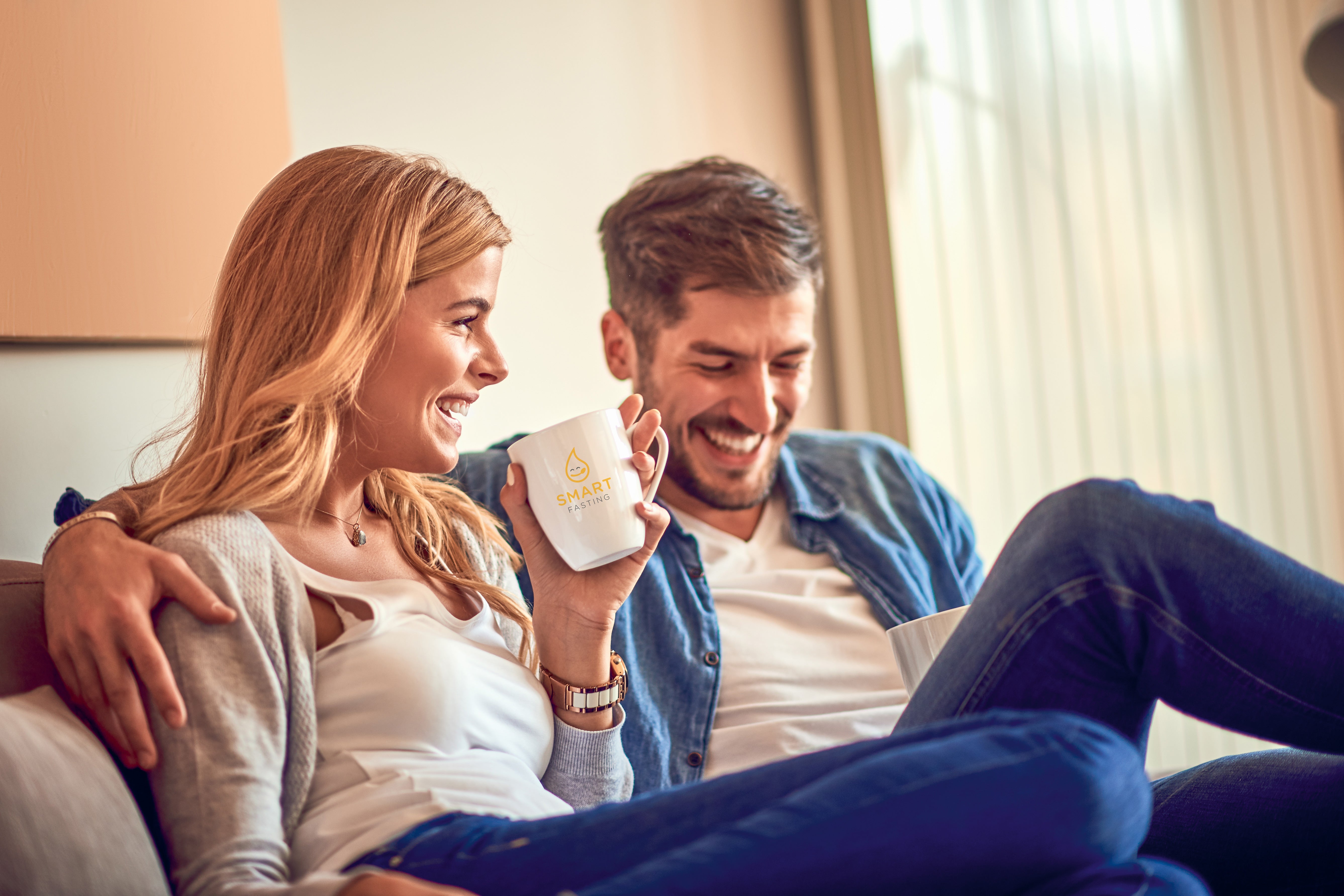 Junges Paar genießt das Heilfasten zuhause mit einer Tasse Smart Fasting Tee auf dem Sofa